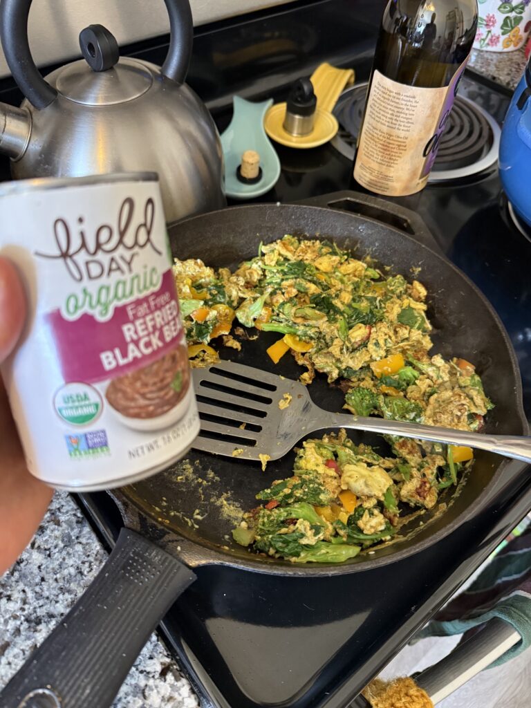 can of refried beans next to cast iron fry pan with scrambled eggs
