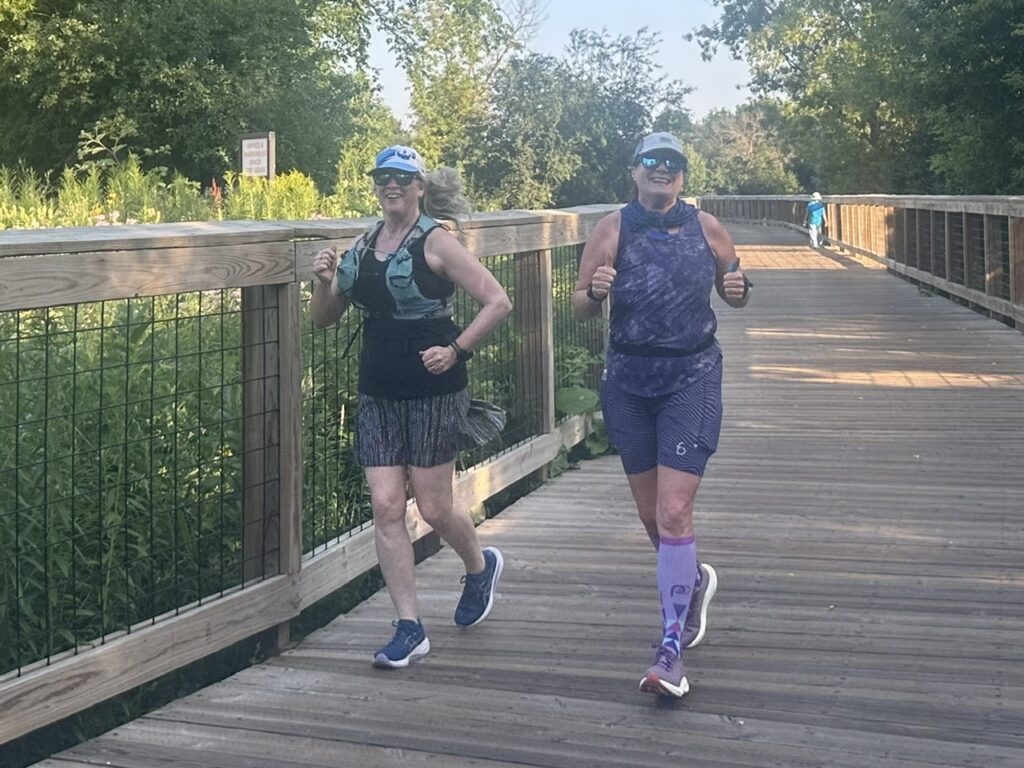 Two runners on a boardwalk smiling. Mari is one of them.